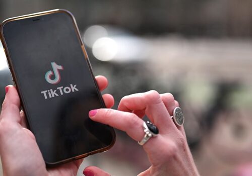 mobile phone with tiktok logo on screen, a hand is pressing the screen