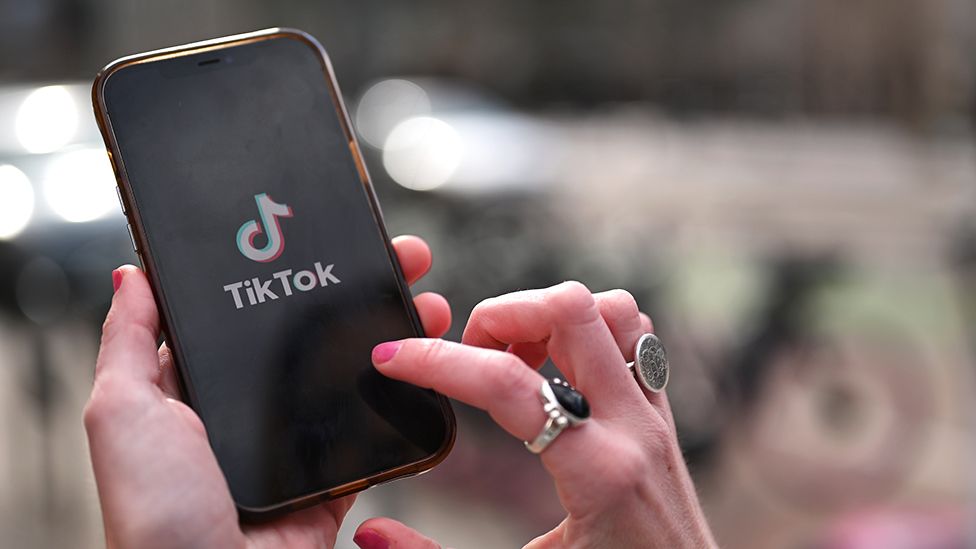 mobile phone with tiktok logo on screen, a hand is pressing the screen